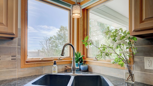 A kitchen with a double sink, wooden cabinets, and a window with a view of trees. - Yellowstone Country Home - Launchpad for a trip of a lifetime!  (Livingston)