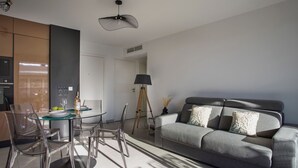 A modern living room with a grey sofa, clear glass chairs, a round glass table, and a ceiling fan. - Le Grey Pearl by Interhome (Cagnes-sur-Mer)