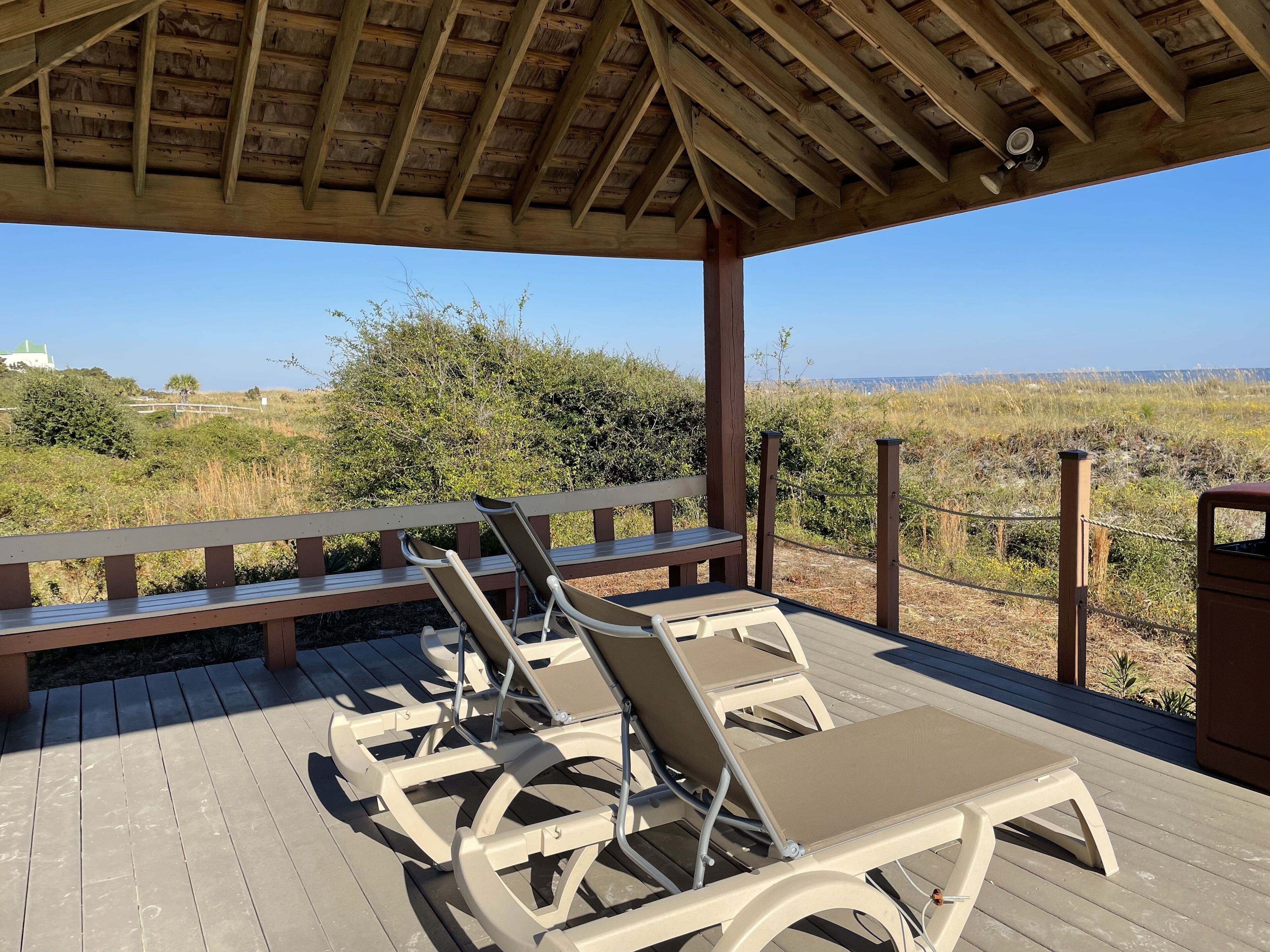 Un espace extérieur aménagé, abrité et doté de bancs en bois et de fauteuils confortables, offrant une vue sur un paysage naturel.