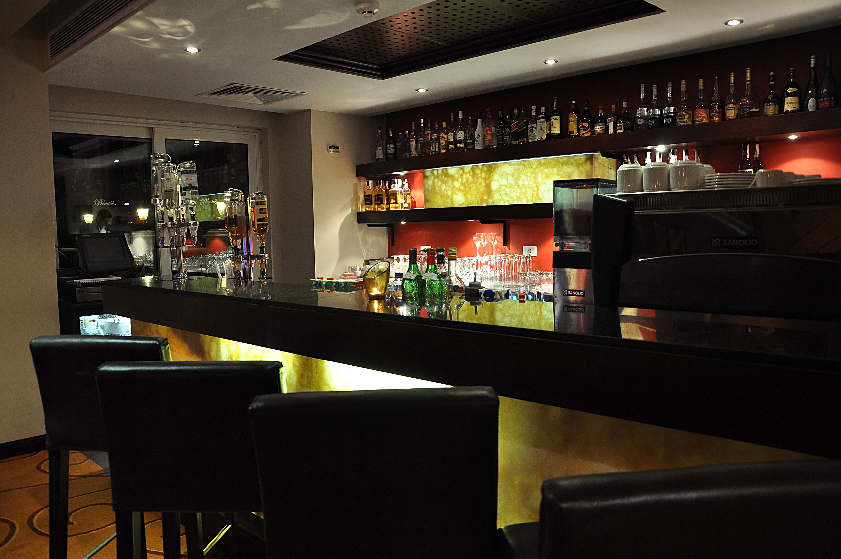 A bar area with a long counter, multiple liquor bottles, glasses, and a coffee machine.