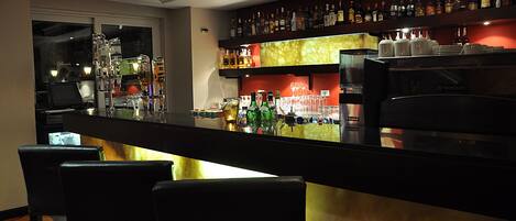 A bar area with a long counter, multiple liquor bottles, glasses, and a coffee machine.