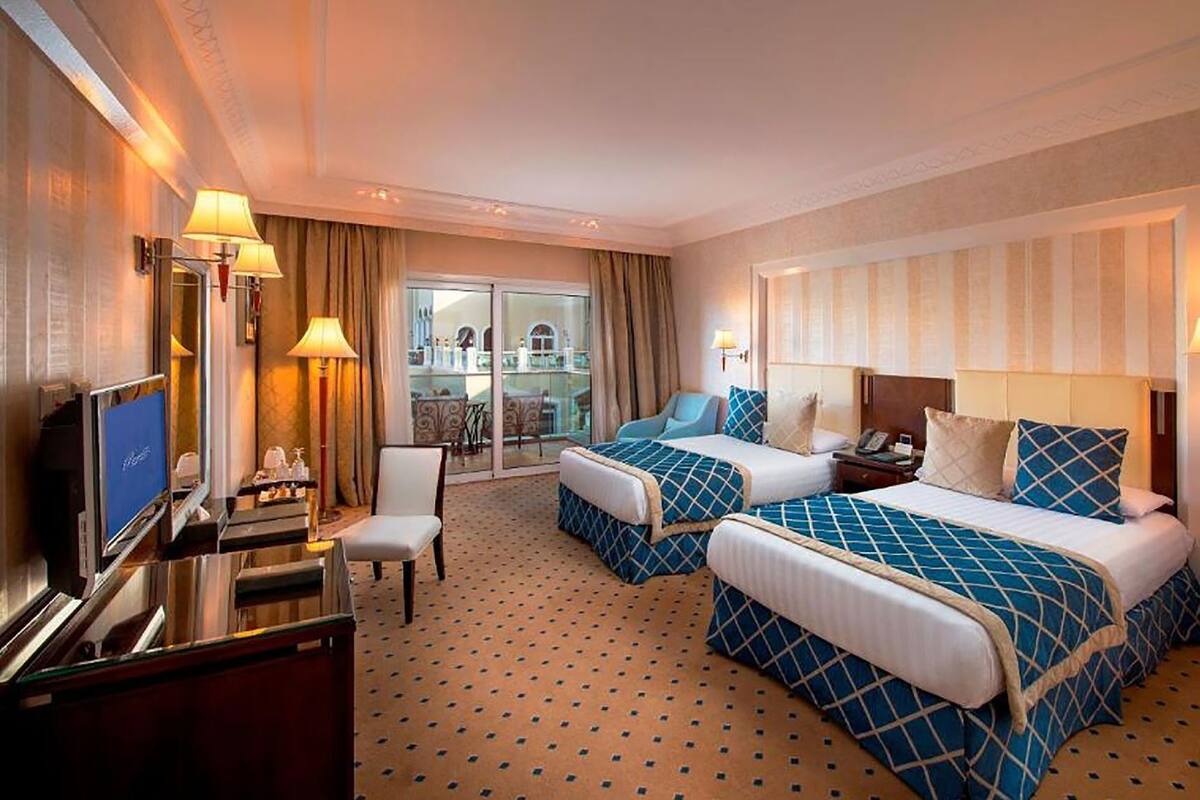 A hotel room with two beds, a TV, a desk, and a balcony with a view.