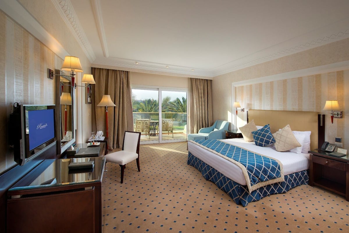 A hotel room with a bed, a desk, a TV, a chair, and a balcony with curtains.