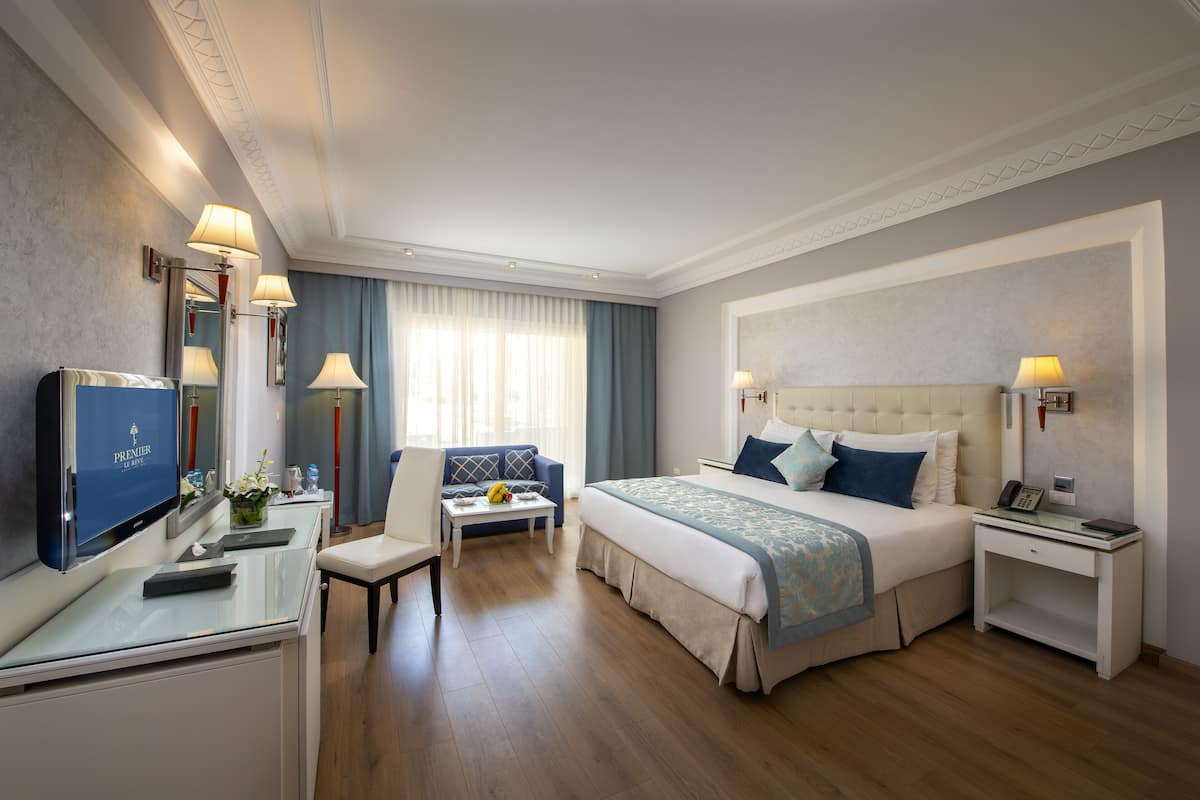 A hotel room with a bed, a desk, a chair, a TV, and a window with curtains.