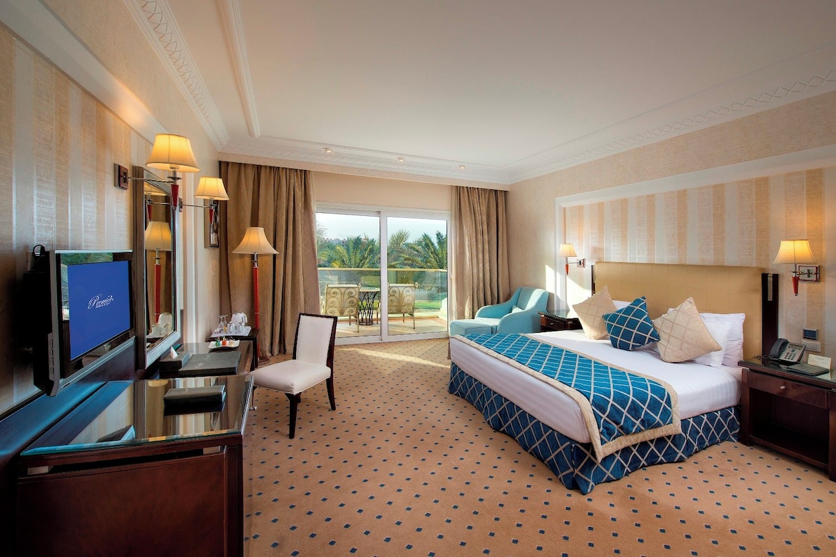 A hotel room with a bed, a desk, a chair, a television, and a balcony with a view.