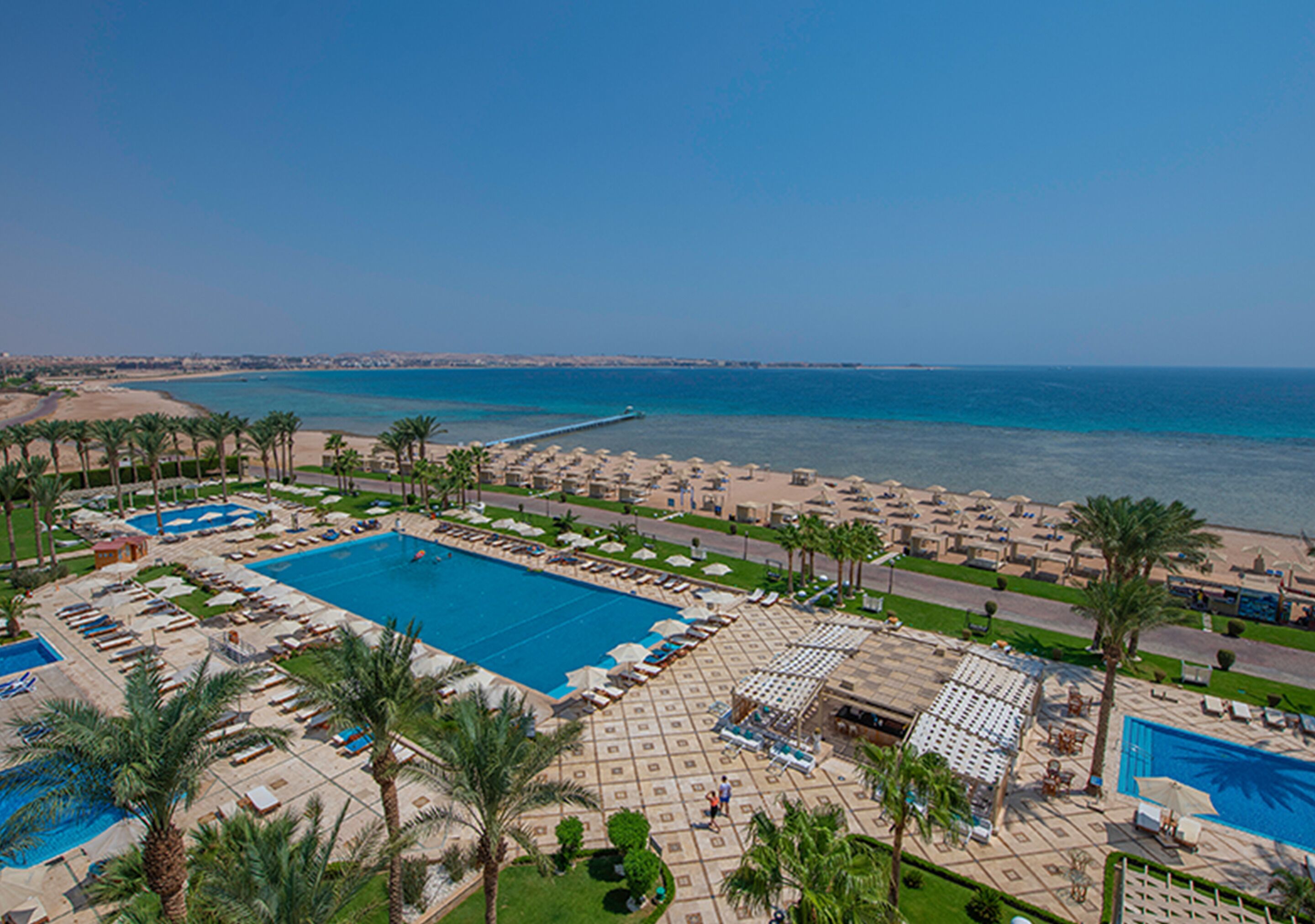 Ein Resort mit großem Pool, Strandbereich und Palmen.