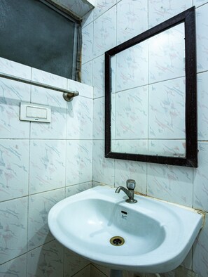 A bathroom with a white sink, a mirror, and a window with a metal screen. - Malar Residencey (Puducherry)