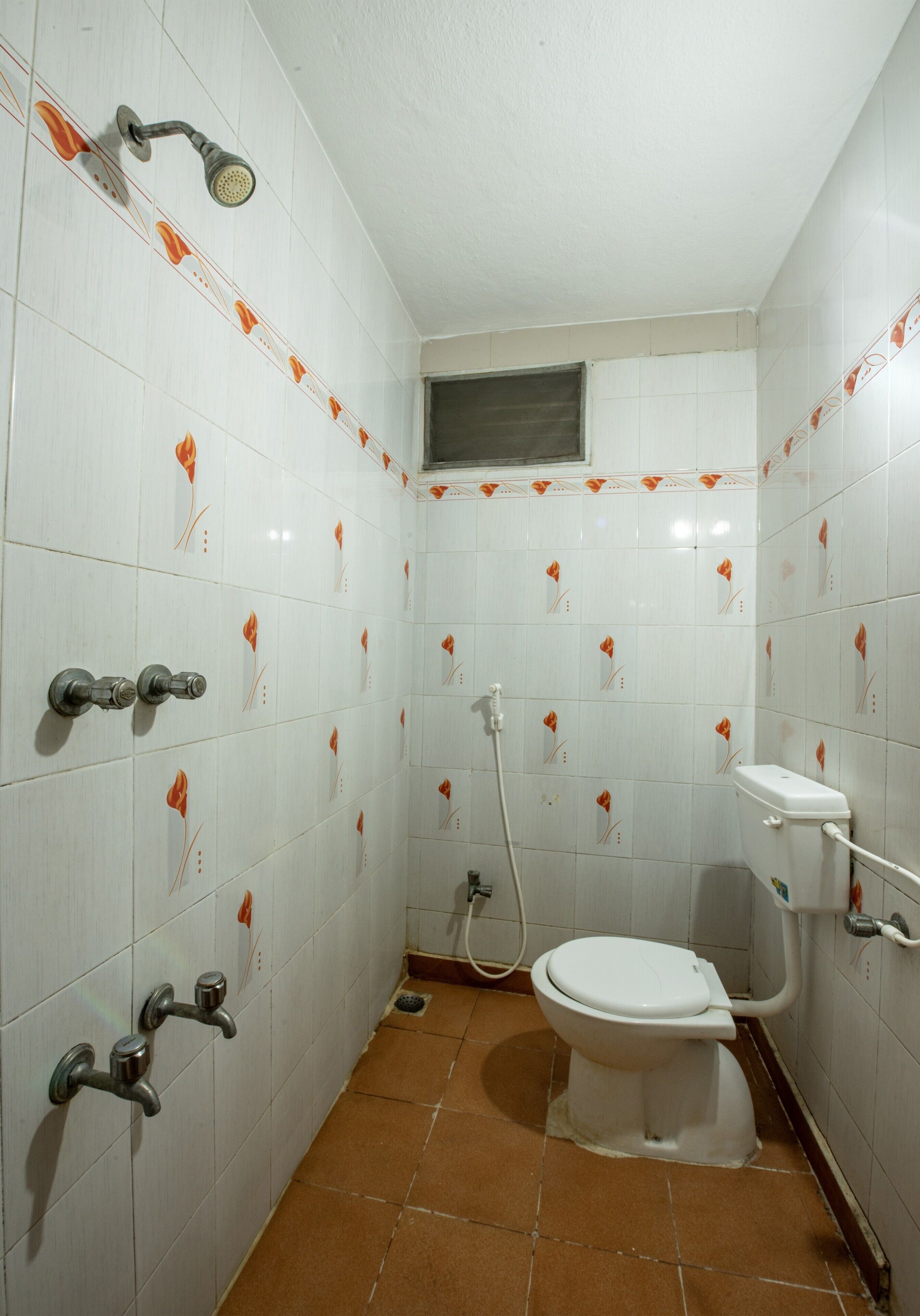 Baño con paredes de azulejos blancos, un inodoro, una ducha y un lavamanos.