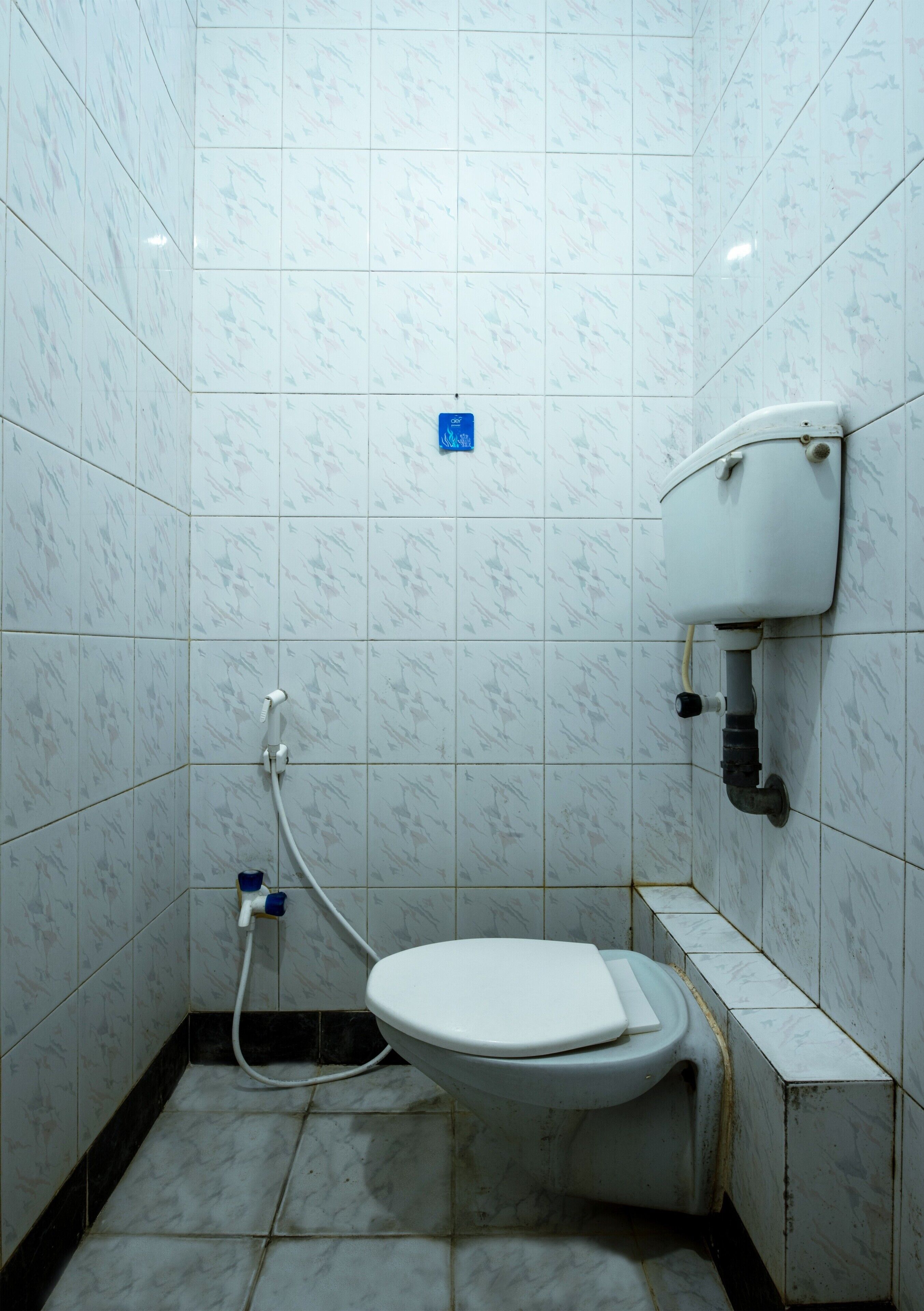 Un baño pequeño con azulejos, que incluye un inodoro, un lavamanos y un dispensador de papel higiénico en la pared.