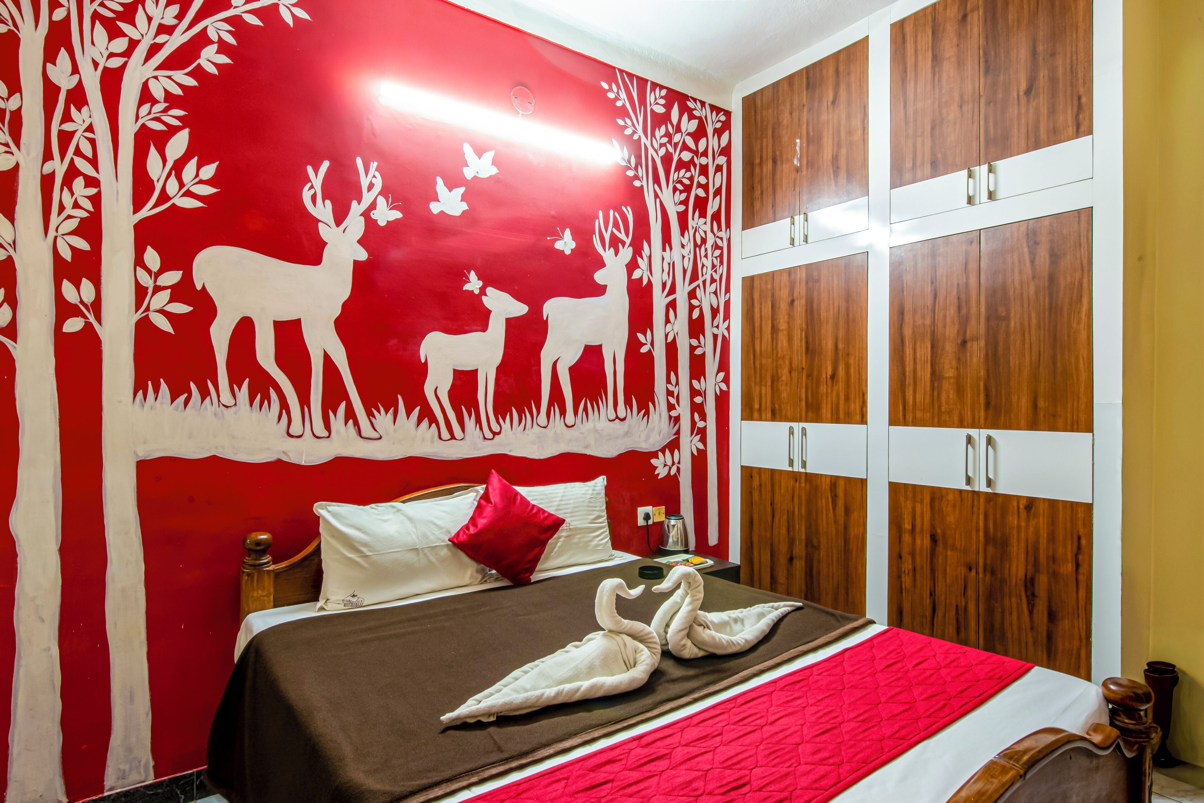 A bedroom with a red wall, a bed with a brown bedspread, a red pillow, and a wooden wardrobe.