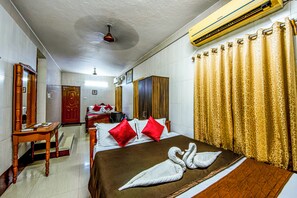 A hotel room with a bed, a desk, a mirror, a wardrobe, and an air conditioning unit. - Malar Residencey (Puducherry)