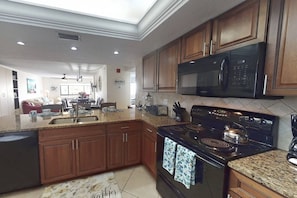 A kitchen with wooden cabinets, a microwave, a stove, and a sink. - Siesta Resort | Private Beach | Gulf Views | Pool (Sarasota)