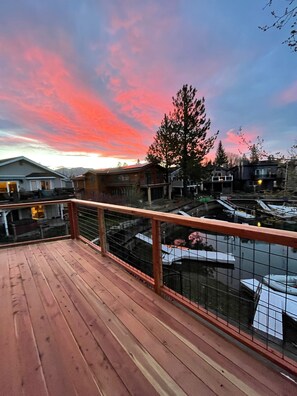 A wooden deck with a metal railing overlooking a residential area with houses and a tree.