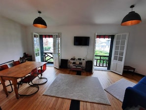 A spacious room with a wooden dining table, chairs, a TV, and a large window.