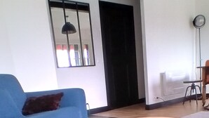 Ein modernes Wohnzimmer mit einem blauen Sofa, einem runden orangefarbenen Pouf und einem weißen Teppich.