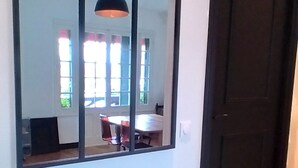 Ein Flur mit einem großen Spiegel, der einen Essbereich, eine schwarze Tür und Holzboden reflektiert.