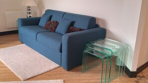 Ein blaues Sofa mit Kissen, ein Glastisch, ein weißer Teppich und eine Lampe.