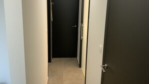 En smal hall med en mörk dörr längst in, en ljusströmbrytare på väggen och ett dörrhandtag på höger sida.