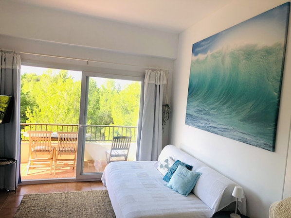 Una stanza con un letto, un quadro raffigurante un'onda, un balcone con sedie e vista sugli alberi.