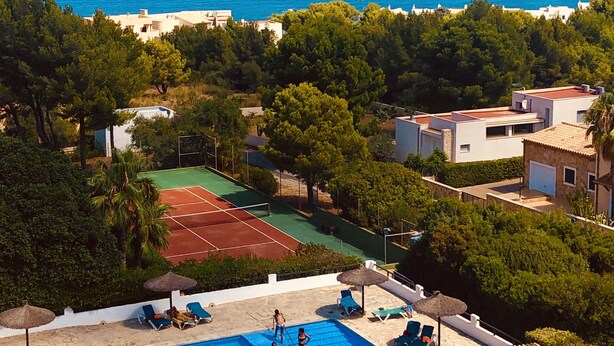 Una piscina con cancha de tenis, vista a la playa y exuberante vegetación.