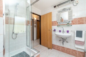 A bathroom with a glass shower enclosure, a sink with a mirror above it, and a wooden door leading to another room. - Vacation House Miramar (Seget)
