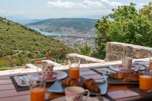 A table set with breakfast items overlooking a scenic view of a coastal town. - Vacation House Miramar (Seget)