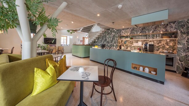 A modern interior with a green sofa, a table, and a bar area with a kitchen in the background. - pradl elf my - apartment (Innsbruck)
