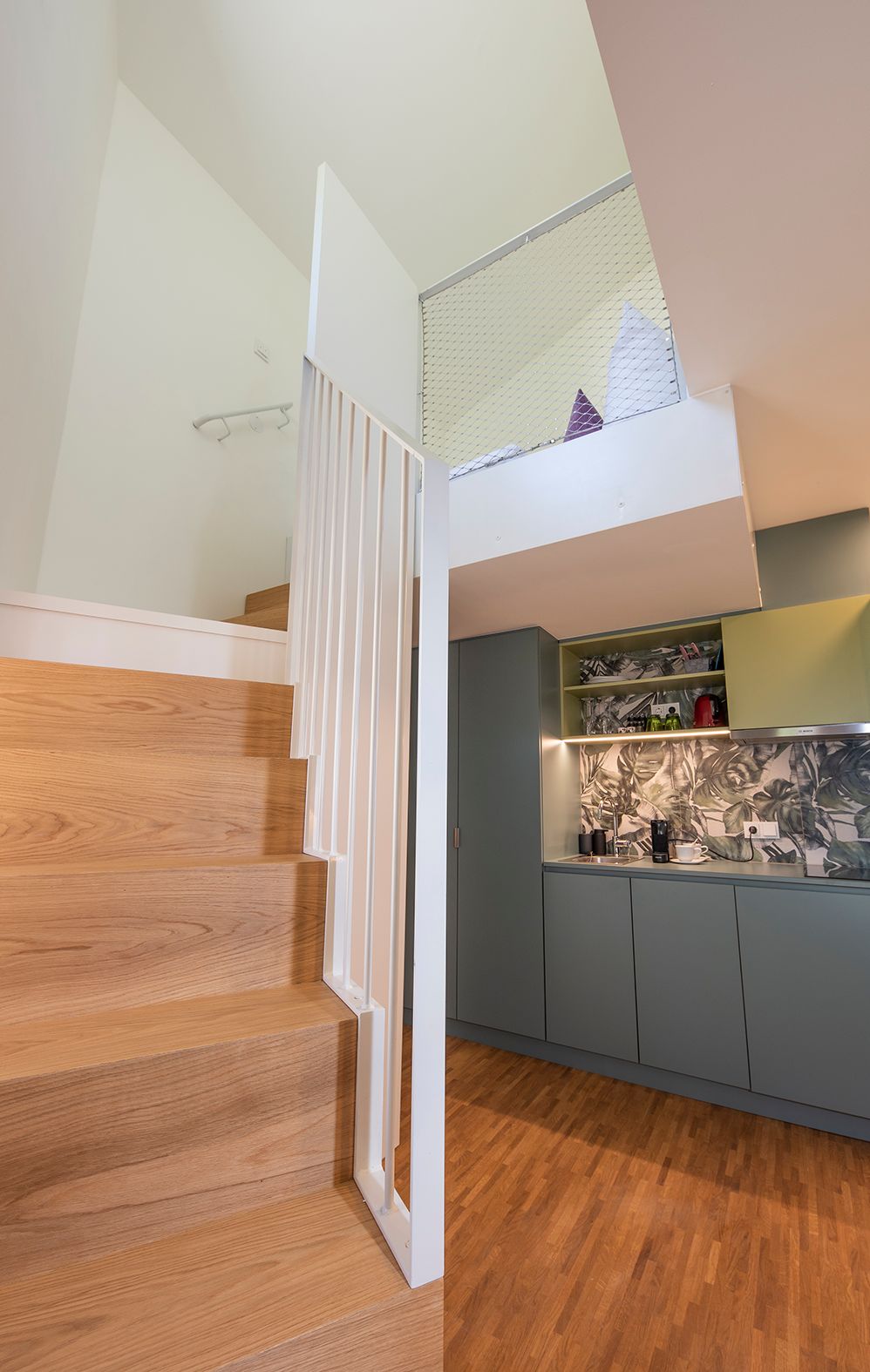 A modern kitchen with grey cabinets, a wooden staircase, and a small dining area.