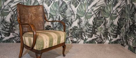 A wooden chair with a striped cushion against a wall with a tropical leaf pattern.