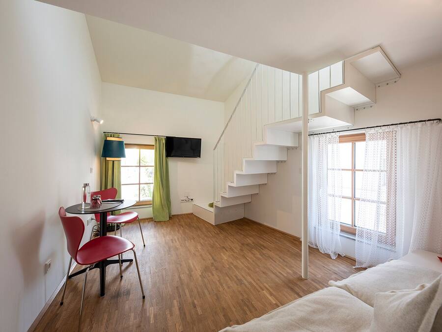 A modern room with a wooden floor, a dining area with a table and chairs, a staircase, and a bed.