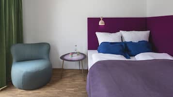 Een kamer met een bed, een stoel, een klein tafeltje en een groen gordijn.