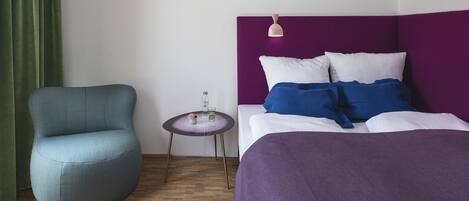 Quarto com cama, uma cadeira, uma mesa pequena e cortina verde.