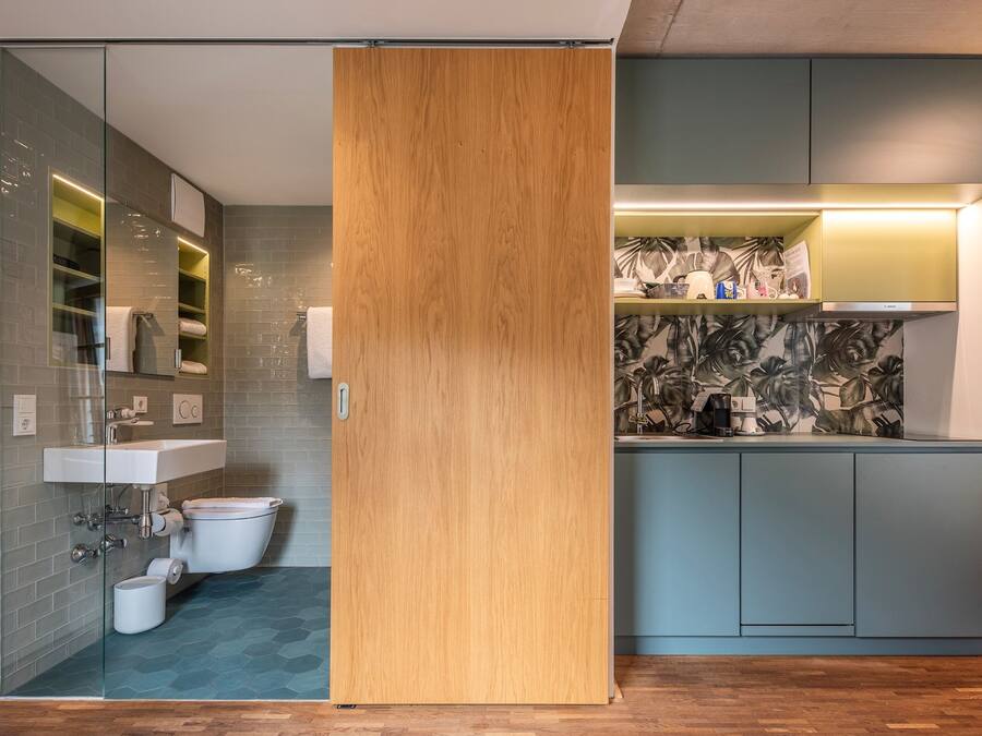 Un baño moderno con cabina de ducha de vidrio, puerta corredera de madera, inodoro y lavamanos.