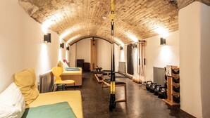 A room with a brick ceiling, a bed with a green blanket, a yellow chair, a table with a red object, and exercise equipment. - pradl elf my - apartment (Innsbruck)