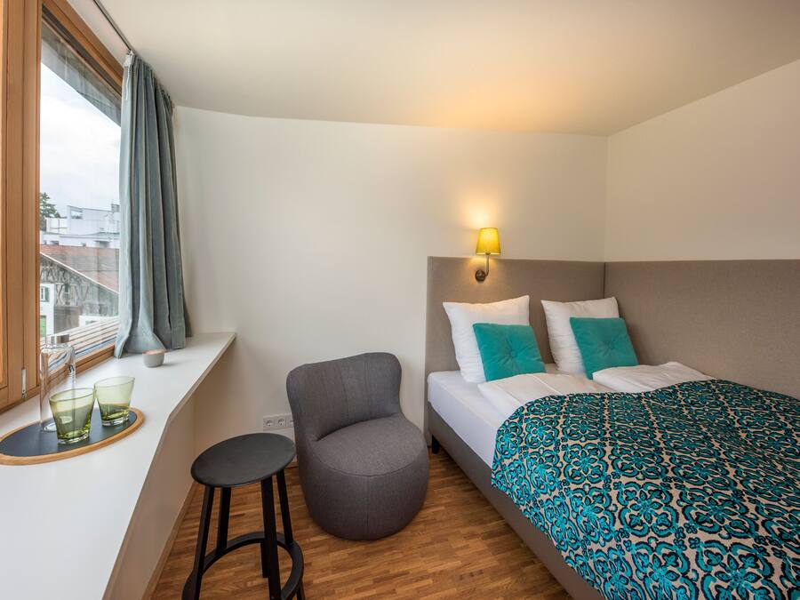Een hotelkamer met een bed, een stoel, een klein tafeltje en een raam met gordijnen.