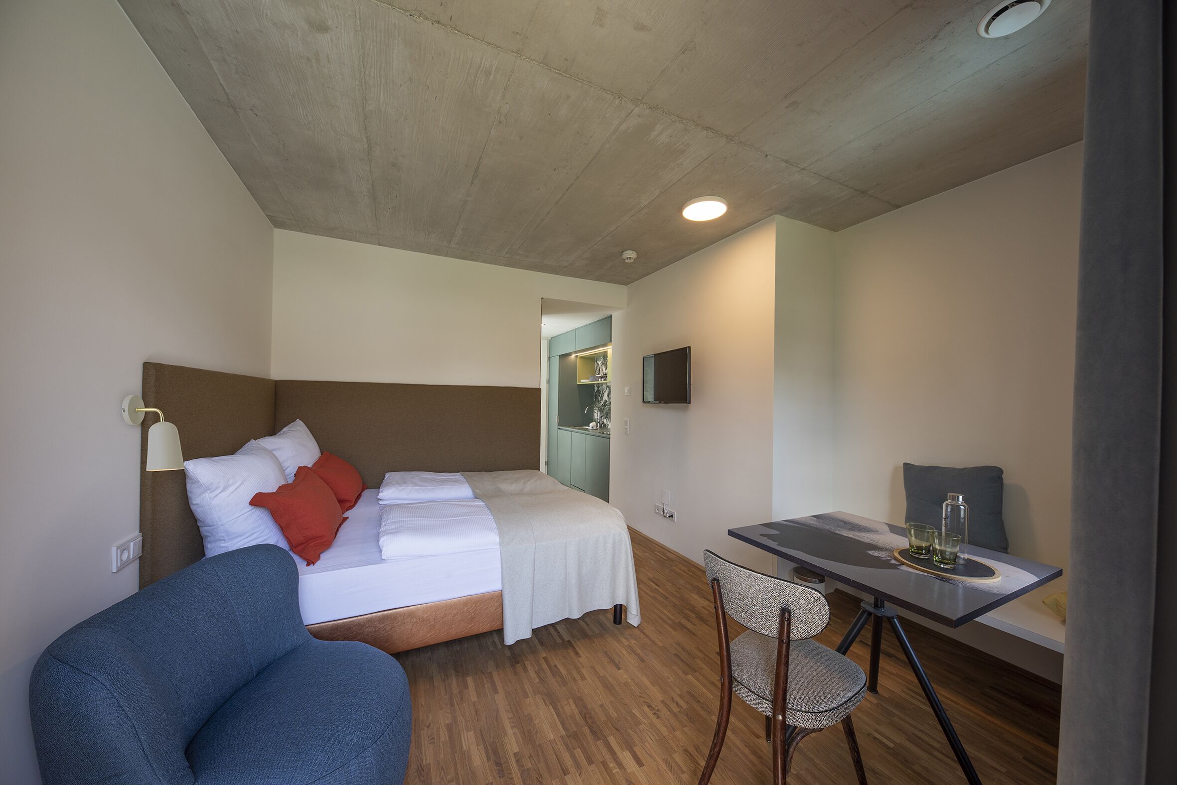 Una habitación de hotel con cama, escritorio, silla y una pequeña kitchenette.