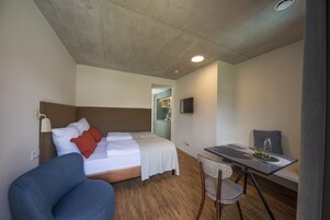 Una habitación de hotel con cama, escritorio, silla y una pequeña kitchenette.