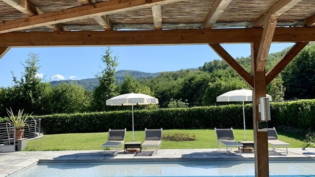 A pool area with a wooden pergola, lounge chairs, and umbrellas. - Welcome to Lush Tuscany and Beautiful Villa Adriano (Borgo a Mozzano)