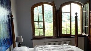 A bedroom with a large bed, two windows with views of greenery, a chandelier, and a radiator. - Welcome to Lush Tuscany and Beautiful Villa Adriano (Borgo a Mozzano)