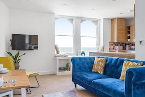 Una sala de estar moderna con un sofá azul, una mesa de comedor de madera y un televisor montado en la pared.