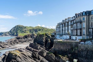 A coastal building with a rocky shoreline and a hill in the background.
