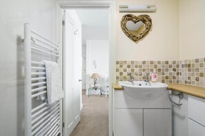 A bathroom with a white sink, a towel rack, a heart-shaped mirror, and a tiled backsplash.