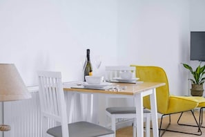A dining area with a table set for two, a bottle of wine, and a television mounted on the wall.