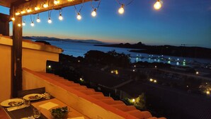 A balcony with a table set for dining, overlooking a marina with boats and a distant shoreline. - Blue Bay Apartment Baja Sardinia (Arzachena)