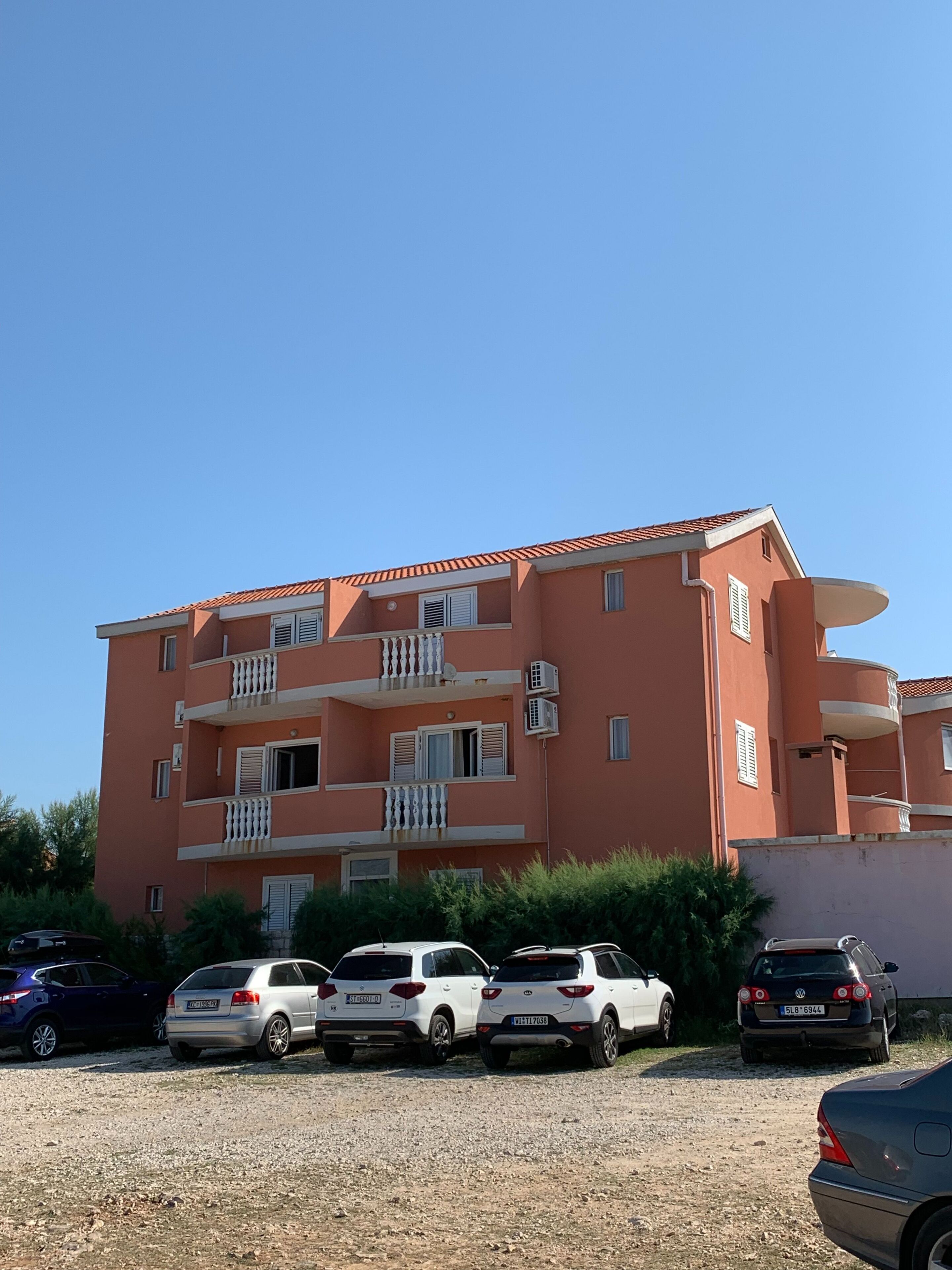A multi-story residential building with balconies and a parking area in front.