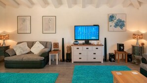 Un salon avec un canapé gris, une petite table d’appoint, un meuble blanc, un téléviseur et deux haut-parleurs.
