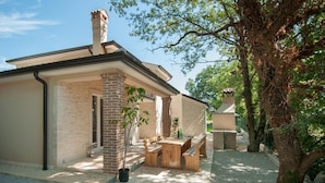 Une maison avec une façade en briques, un patio couvert avec des meubles en bois et un arbre au premier plan.