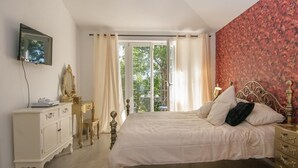 Une chambre à coucher avec un lit, une commode, un miroir et une fenêtre avec des rideaux.