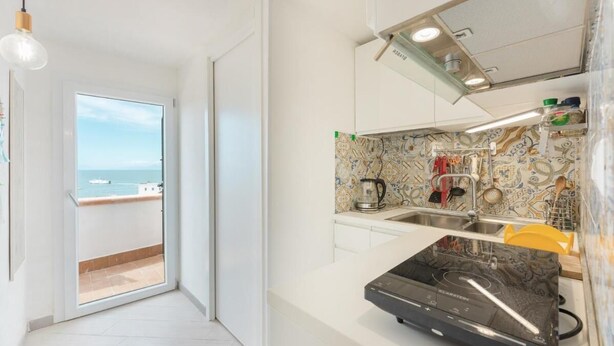A modern kitchen with a large window, a built-in stove, and a view of the sea. - Terramare Guesthouse (Procida)