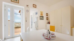 A room with a white table set for tea, a view of the sea through a glass door, and a wardrobe with a mirror. - Terramare Guesthouse (Procida)